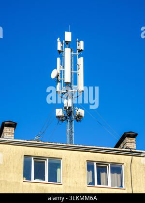 Mobile network antenna tower installed on apartment building rooftop under clear blue summer sky view Stock Photo