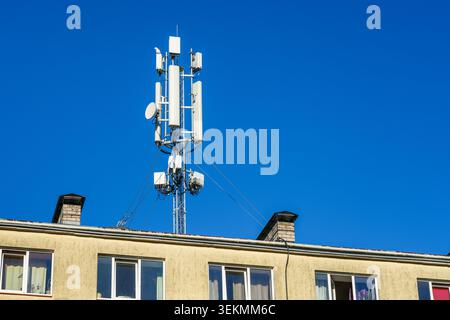 Cellular communication tower mounted on residential building rooftop against clear blue sky backdrop Stock Photo