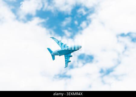 A small toy airplane flying across a bright summer sky with soft white clouds. Copy space. Stock Photo