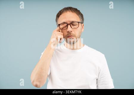 Eye problem. Tired man feels irritated rubbing dry eyelids for relief vision pain isolated studio. Male wearing eyeglasses suffer bad blurry vision by Stock Photo