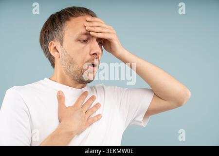 Stressed man with panic attack holding head, chest in distress tries to regain control. Anxious male with difficult breathing, rapid heartbeat feels e Stock Photo