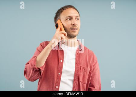 Interesting conversation. Focused man holds smartphone to ear to answer call. Smiling thoughtful guy talking on phone at leisure, discussing pleasant Stock Photo