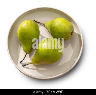 Overhead flat lay studio shot of three fresh organic green pears arranged on a light-colored decorative ceramic plate. Captured in bright, warm, sunny Stock Photo