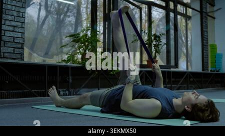 Young man lying on fitness mat performing resistance band leg exercise Stock Photo