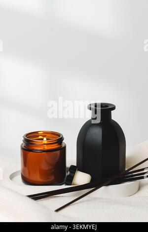 Scented candle and diffuser on a white surface near a beige fabric in a cozy setting Stock Photo