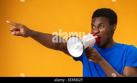 Person shouts through megaphone while pointing in a studio with orange background Stock Photo