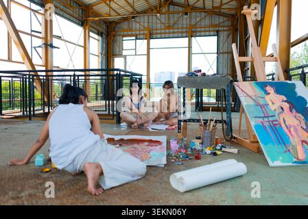 Three young women creating art in an open studio, painting and posing Stock Photo