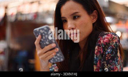 Young woman focusing on smartphone screen, browsing content outdoors Stock Photo