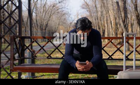 Pensive thoughtful young guy sitting on bench looking down sadly Stock Photo