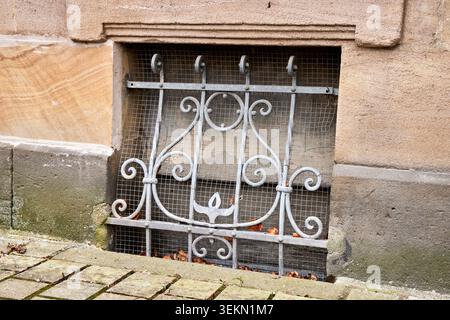 Vintage ornate forged iron security bars protecting a basement window of an old stone building. Stock Photo