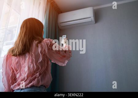 Woman adjusts split system air conditioner with remote control, cooling a sunny apartment for comfortable indoor climate and energy efficient relief Stock Photo