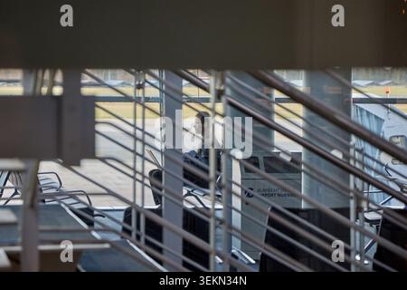 Passenger working on laptop in airport terminal waiting area seen through stairs structural elements. Stock Photo