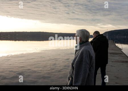 Elderly short haired woman spending leisure time with man while standing on pier near river Stock Photo