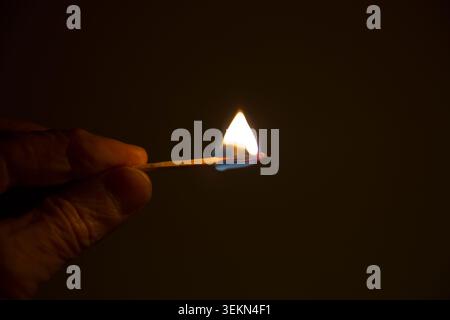 Hand on unrecognizable person holding burning matchstick in dark Stock Photo