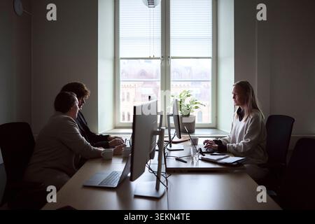 Concentrated female and male business expert working on technologies while sitting at desk in office Stock Photo