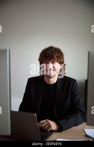Portrait of smiling male business professional sitting in office at desk Stock Photo