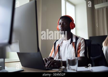 Concentrated male programmer wearing wireless headphones working on technologies in office Stock Photo