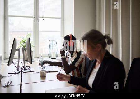 Male tech expert wearing wireless headphones while working on computer in office Stock Photo