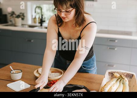 Young woman making breakfast while standing near table in home kitchen Stock Photo