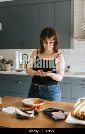 Young woman making breakfast while standing near table in kitchen at home Stock Photo