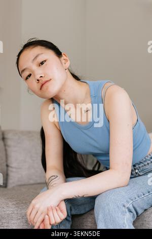 Portrait of confident young woman posing while sitting on sofa at home Stock Photo