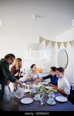 Family having cake while sitting around dining table during birthday celebration at home Stock Photo