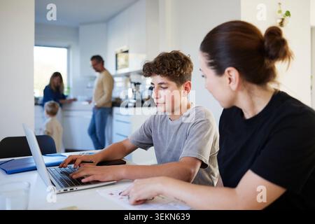 Boy using laptop for studies while sitting next to mother at home Stock Photo