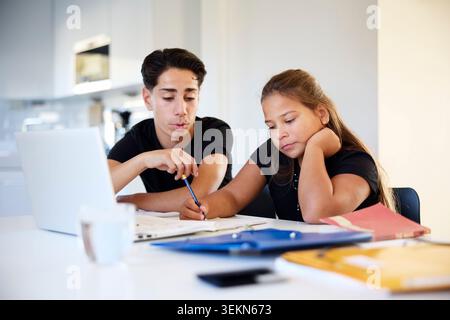 Girl doing her homework while sitting next to brother at home Stock Photo
