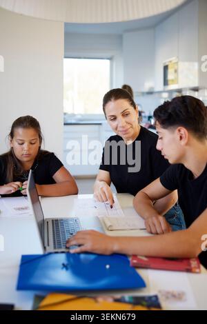 Smiling woman helping her children while studying at home Stock Photo