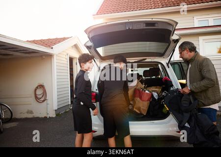 Father and sons loading bags in car trunk Stock Photo