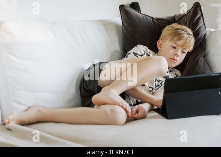 Full length of boy using digital tablet while resting on sofa at home Stock Photo