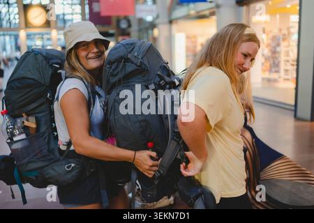 Happy female tourists with backpacks standing at railway station Stock Photo
