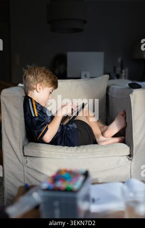 Side view of boy using digital tablet while sitting on sofa at home Stock Photo