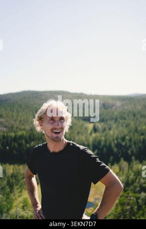 Happy man looking away while standing with arms akimbo against rural landscape Stock Photo