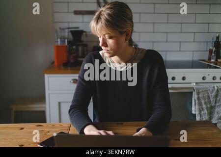 Businesswoman checking notifications on her smart phone while working on laptop at home Stock Photo