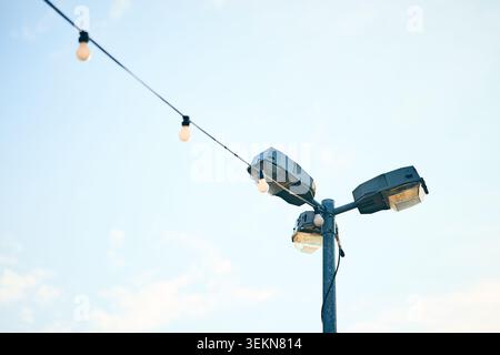 A tall pole with mounted floodlights and a diagonal strand of hanging bulbs shown against a clear bright sky, creating a simple outdoor lighting scene Stock Photo