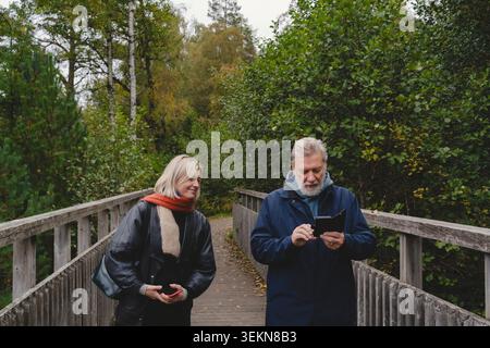 Senior man using smart phone while walking on bridge with daughter at park Stock Photo
