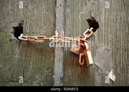 Rusty chain and two padlocks securing an old weathered wooden door. Stock Photo
