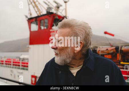 Thoughtful senior man looking away with ferry boat in background at harbor Stock Photo