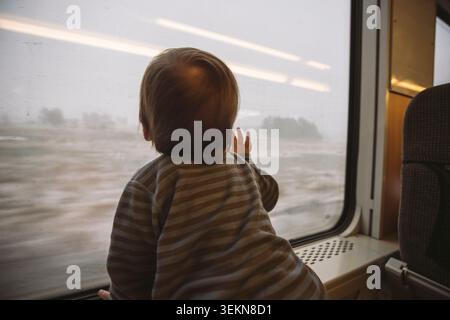 Rear view of boy looking through train window Stock Photo