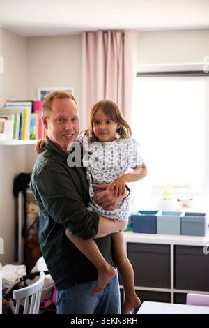 Portrait of father carrying daughter in arms while standing in bedroom Stock Photo