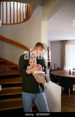 Father embracing baby boy while standing near steps in home Stock Photo