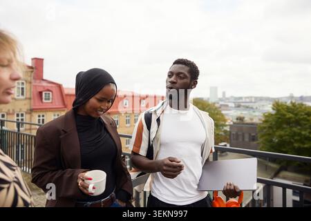Young businessman holding laptop and discussing with colleagues on office terrace Stock Photo