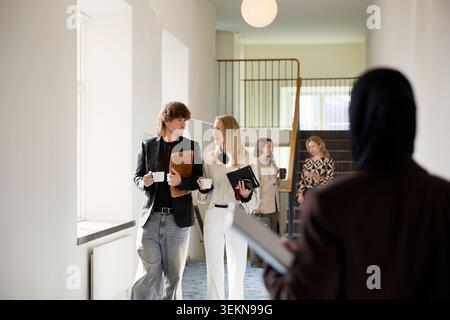 Male and female business professionals talking while walking in corridor during coffee break Stock Photo