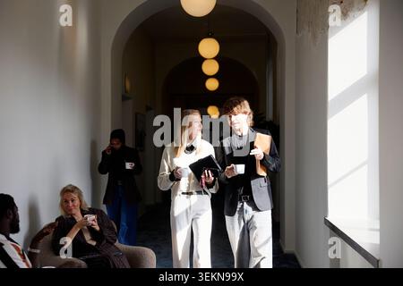 Male and female business professionals discussing during coffee break while walking in illuminated corridor Stock Photo