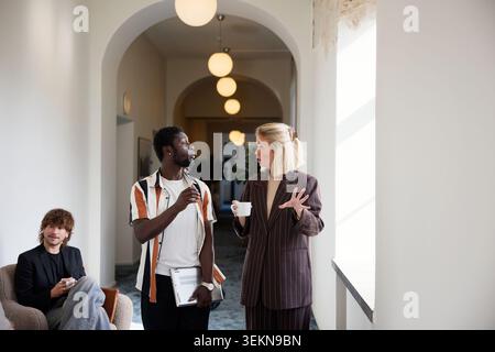 Male and female entrepreneurs sharing business ideas while walking in illuminated corridor Stock Photo