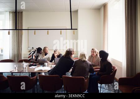 Male and female business professionals sharing marketing ideas while sitting in office meeting room Stock Photo