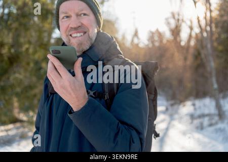 Smiling man talking through speaker phone while traveling in winter Stock Photo
