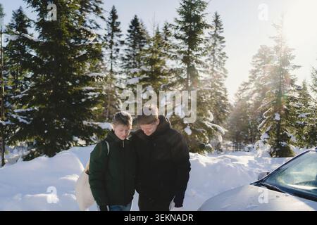 Man and woman dressed in warm clothes standing by car in winter forest Stock Photo