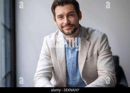 Portrait of smiling male business entrepreneur wearing blazer sitting in office Stock Photo